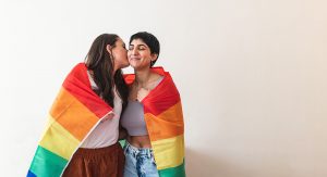 Happy lesbian couple wrapped in rainbow flag and giving a kiss